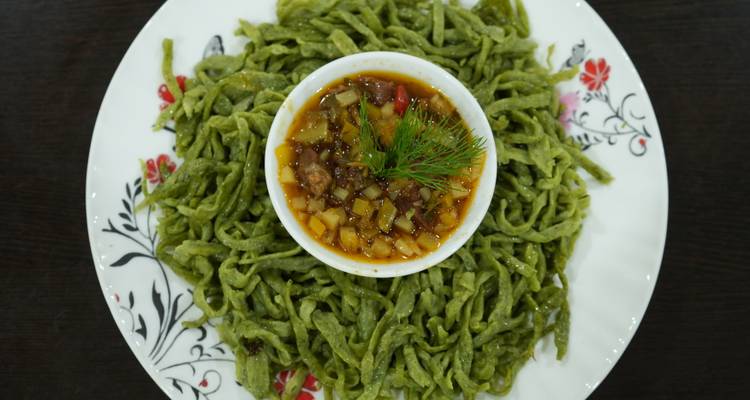 Uzbek green hand-cut noodles arranged around a bowl of hearty stew garnished with dill.