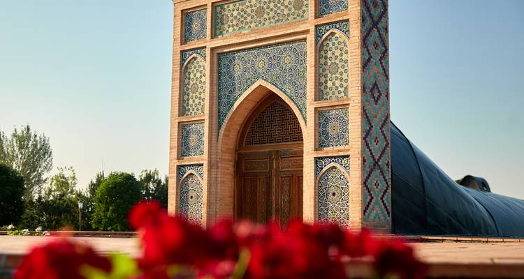 Decorative tiled portal of an Uzbek mausoleum with red flowers blurred in foreground.