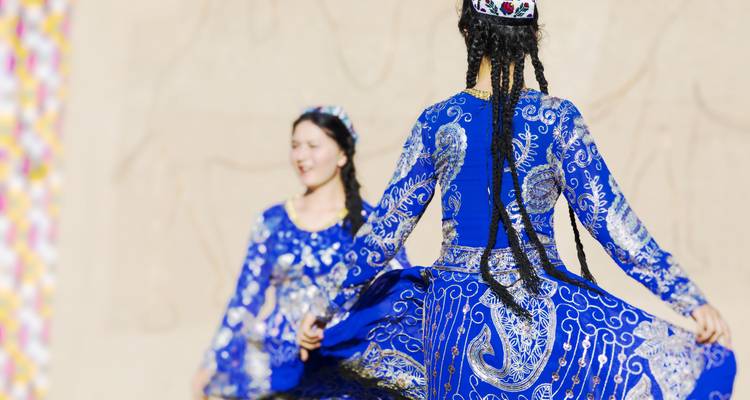 Two women in bright blue traditional dresses spin gracefully during a folk dance performance.