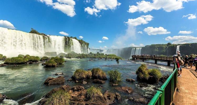 Vista de las Cataratas del Iguazú desde un río con turistas en una pasarela.