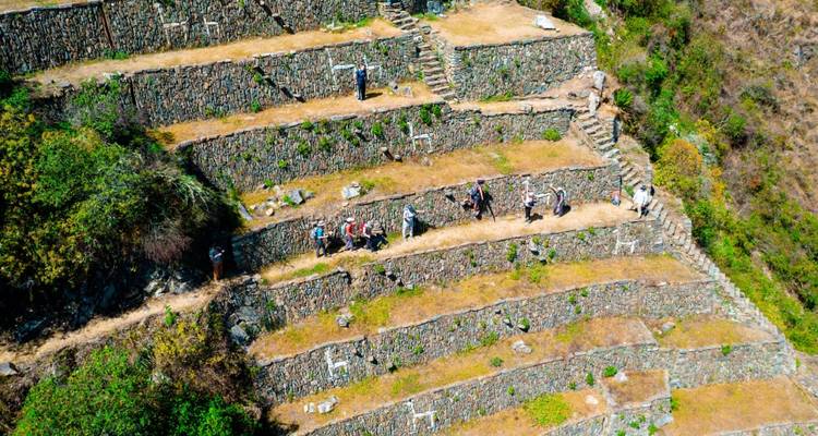 Excursionistas caminando a lo largo de laderas con terrazas de ruinas.