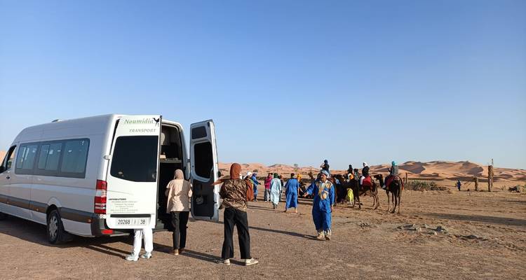 Los turistas se reúnen junto a un minibús del desierto preparándose para una caravana de camellos en medio de vastas dunas de arena.