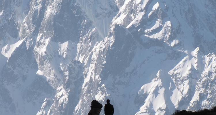 A silhouette of a person in front of a towering snow-covered mountain.
