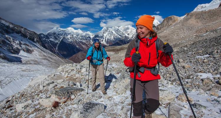 Two hikers with trekking poles walking on a snowy mountain path.