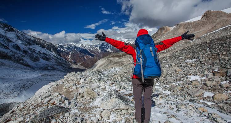 A person standing with arms outstretched on a rocky path, overlooking a mountainous landscape.