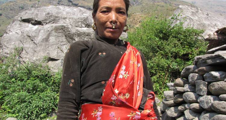 A woman wearing a vibrant red garment, standing outdoors in a mountainous setting.
