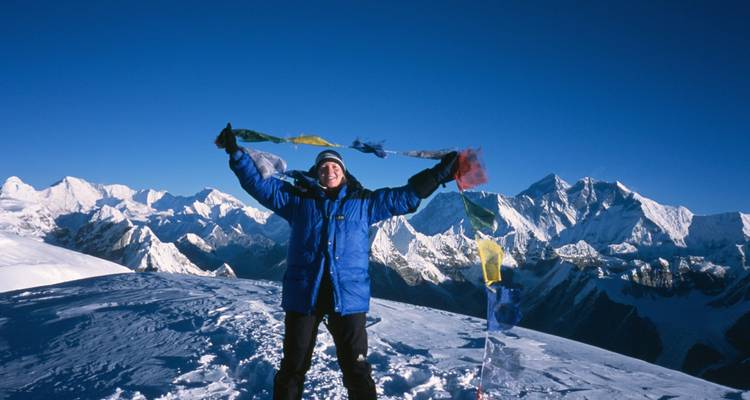Person on top of a snowy peak with colorful flags.
