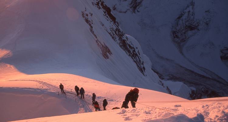 Climbers ascending a snowy mountain in early light.