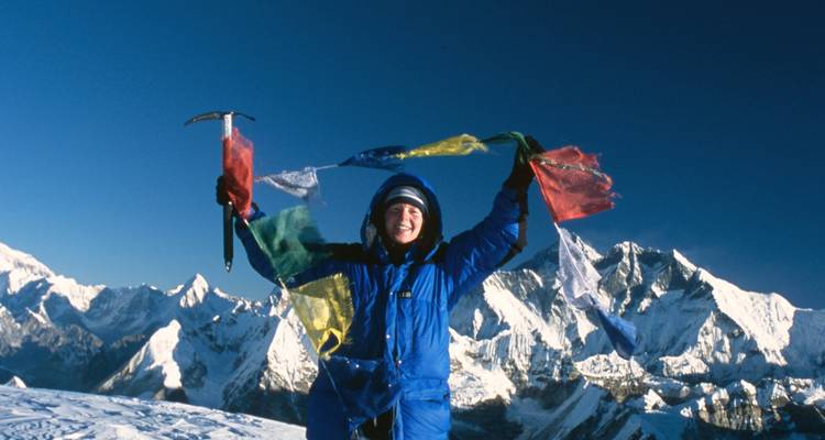 Person posing on a snowy mountain with prayer flags.