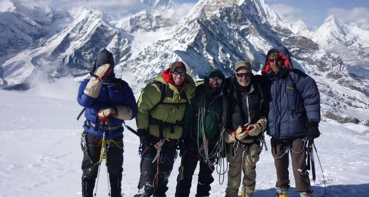 Group of mountaineers posing with snowy peaks in background.