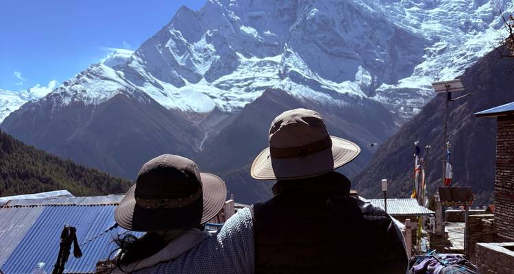Una pareja con sombreros de ala ancha admira imponentes paredes de nieve y glaciares desde el balcón de un albergue.