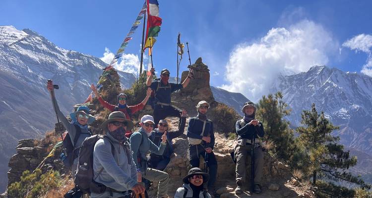 Los trekkers izan banderas de oración en un mirador rocoso enmarcado por picos cubiertos de nieve y nubes que soplan.