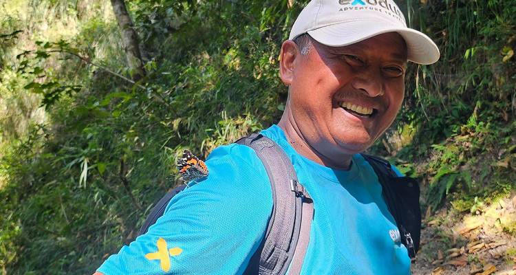 Un guía alegre sonríe mientras una mariposa descansa en su hombro durante una caminata por la selva.