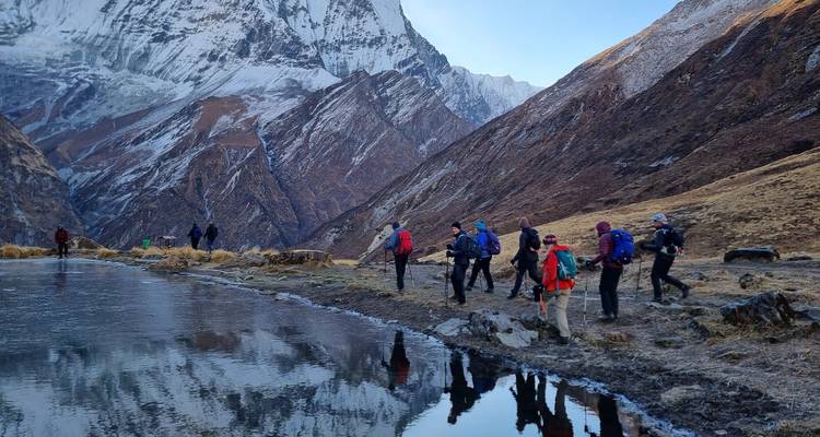 Trekker umgehen einen gefrorenen See, der schneebedeckte Gipfel in der Nähe des Annapurna Basislagers widerspiegelt.