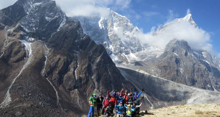 Un groupe de randonneurs fêtant sur une crête avec de grands sommets enneigés en arrière-plan.