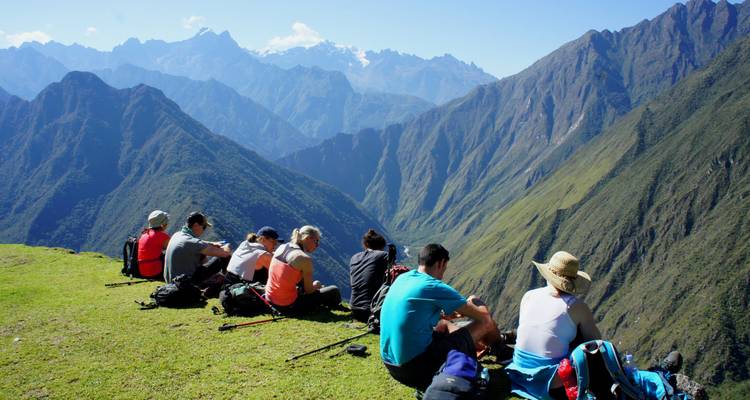 Grupo de excursionistas sentados admirando un impresionante paisaje de montaña.