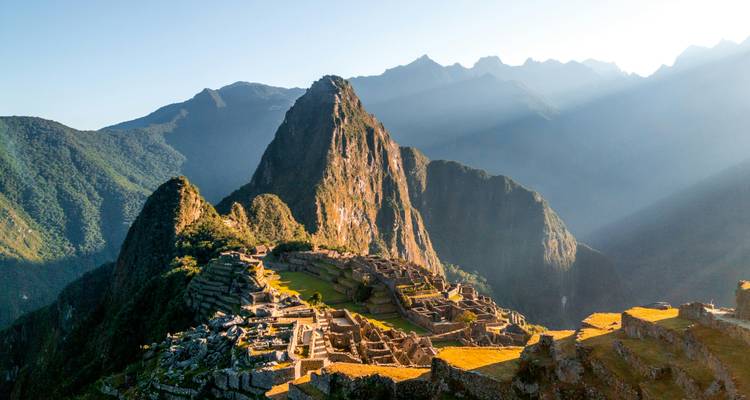 Iconic sunrise view of Machu Picchu citadel with sunbeams over the surrounding Andes.