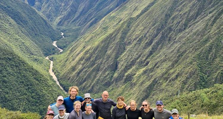 Large hiking group poses on a ridge overlooking a deep river valley in the Andes.