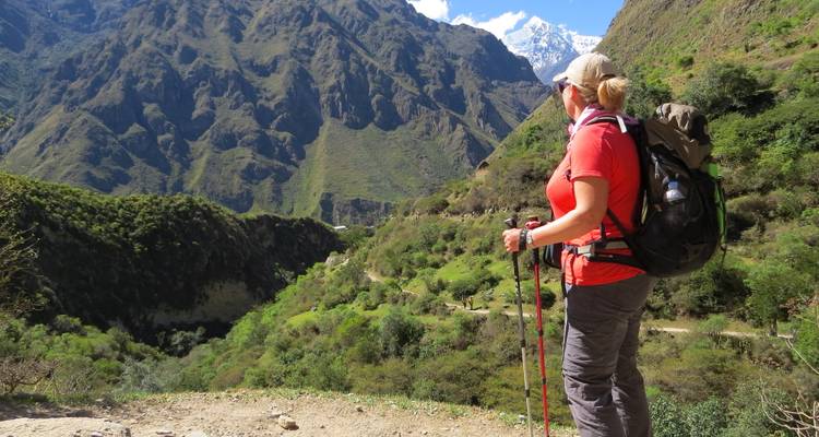 Female backpacker gazes over a dramatic green canyon with snow-capped peak ahead.