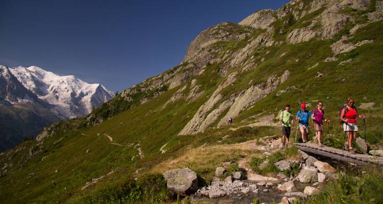 Randonneurs traversant un pont sur fond de montagne.