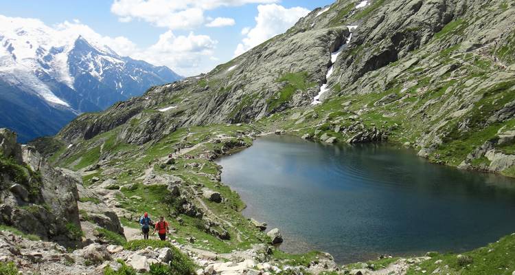 Randonneurs près d'un lac de montagne avec des sommets enneigés.