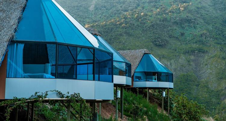 Modern glass-fronted dome cabins cling to a green mountainside in the Andes.