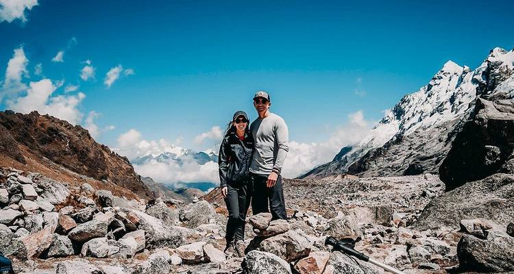 Smiling couple pose amid a rocky glacier moraine with snowy Andean peaks behind.