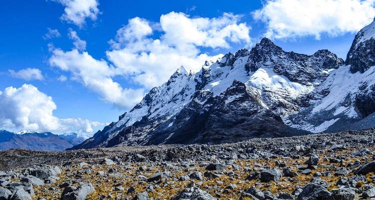 Wide view of rocky high-altitude plateau backed by snow-covered peaks under scattered clouds.