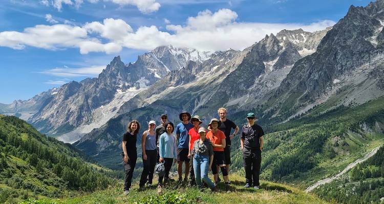 Een wandelgroep staat op een grassige bergrug met het sneeuwbedekte Mont Blanc-massief dat achter hen uittorent.