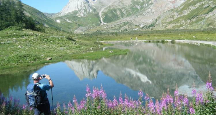 Homme prenant une photo près d'un lac réfléchissant avec des montagnes en arrière-plan.