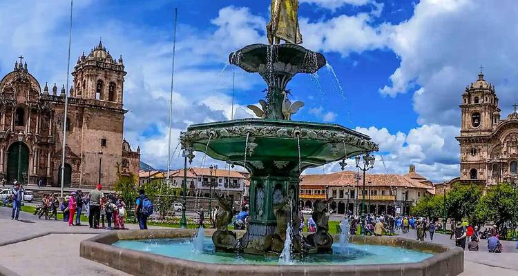 Fuente en una plaza animada con edificios históricos y gente alrededor.