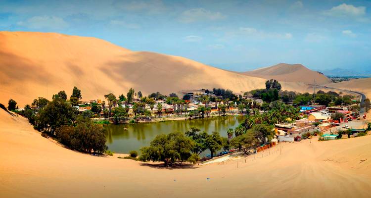Pueblo oasis rodeado de vegetación exuberante y dunas de arena.