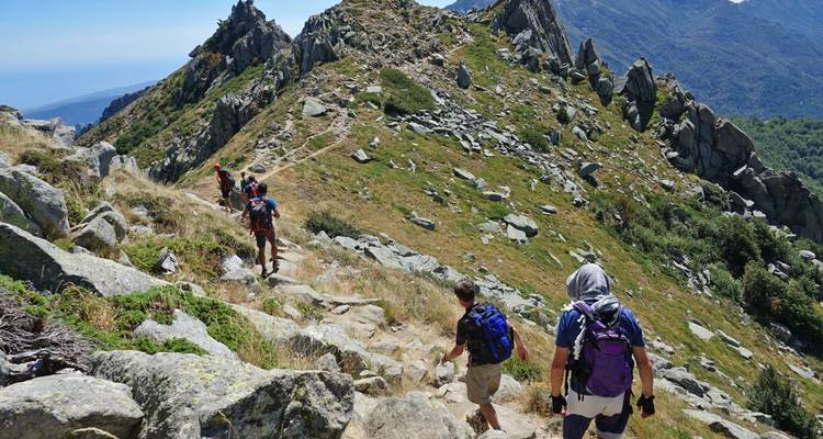 Los excursionistas suben por una afilada cresta montañosa llena de rocas bajo un cielo azul despejado