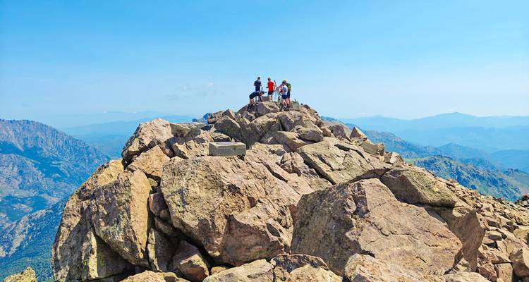 Grupo de excursionistas de pie en una cumbre rocosa con vistas montañosas expansivas por todas partes