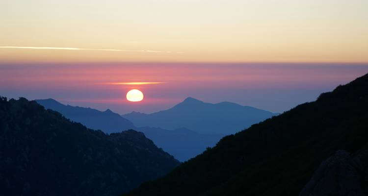 Atardecer minimalista con el sol descendiendo detrás de las crestas de las montañas silueteadas