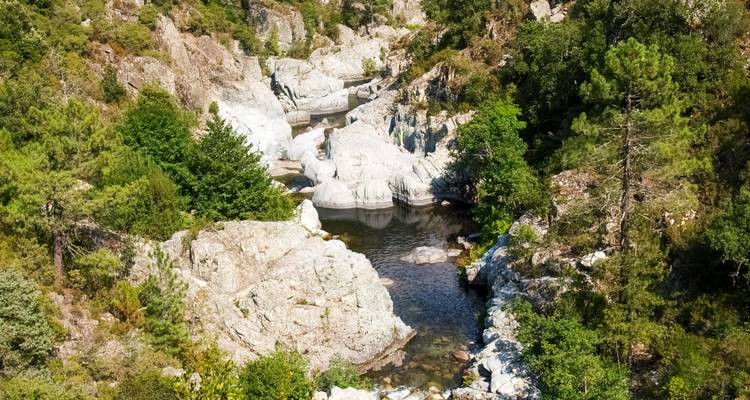 Pequeña piscina natural de roca rodeada de bosque y formaciones de granito en un valle corso