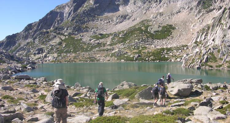 Grupo de excursionistas cerca de un lago de montaña rodeado de terreno rocoso.