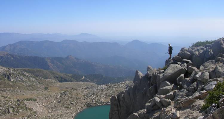 Vista lejana de un excursionista en un acantilado rocoso con vistas a un lago.
