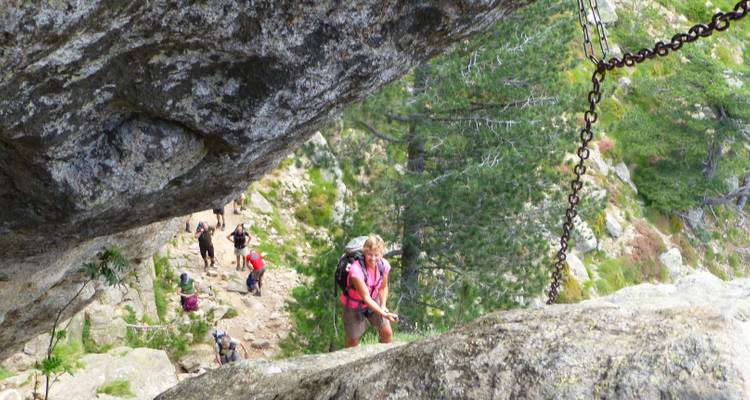 Senderista escalando por terreno rocoso utilizando cadenas.