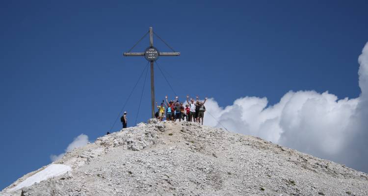 Grupo de pie bajo una cruz en la cumbre con nubes detrás.
