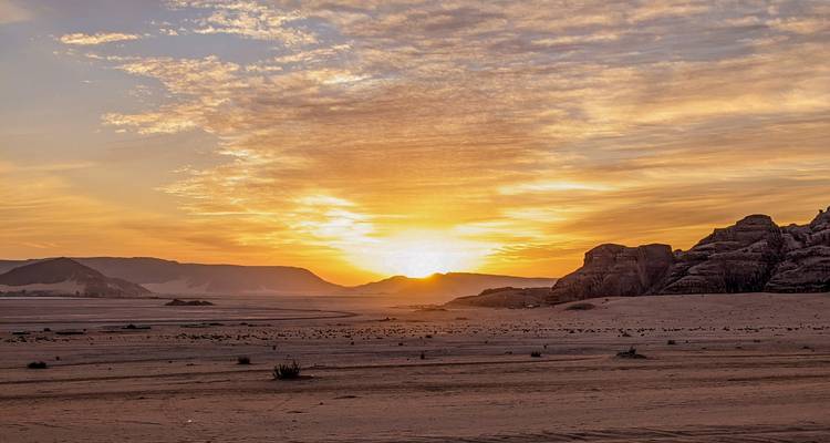 Gouden zonsopgang giet licht over lege woestijnvlaktes en verre zandsteenbergen.