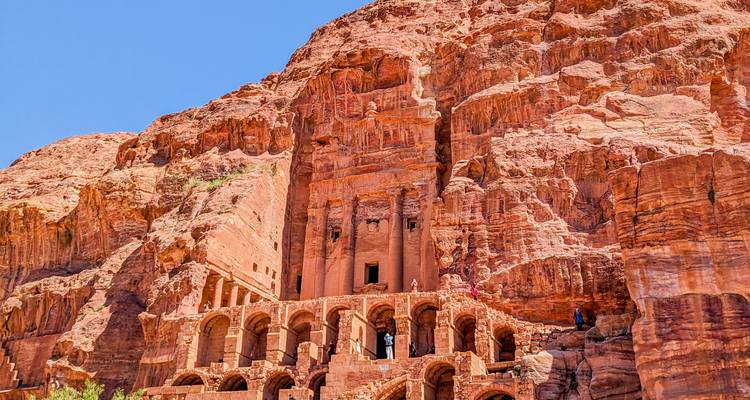 Des tombes royales impressionnantes taillées dans la roche s'élèvent des falaises rouges de Pétra sous un ciel dégagé.
