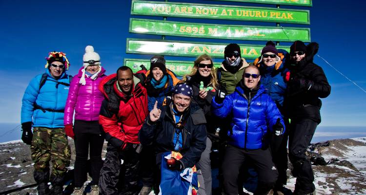Eine größere Gruppe feiert am Gipfelschild des Uhuru Peak.