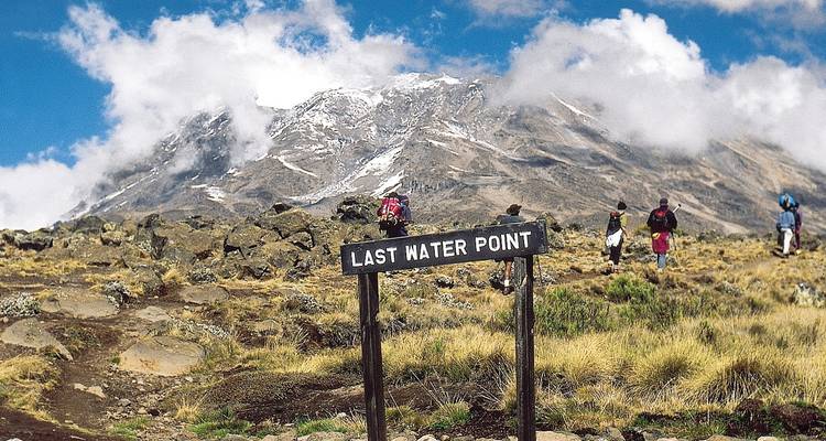 Wanderer, die sich einem Berg nähern, der mit 'Last Water Point' markiert ist.