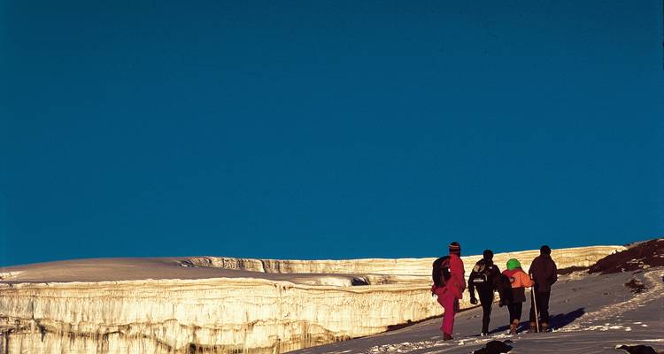 Menschen, die durch eine verschneite Landschaft mit Gletschern laufen.