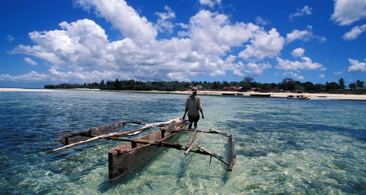 Eine Person steuert ein traditionelles Holzboot durch das klare blaue Wasser.