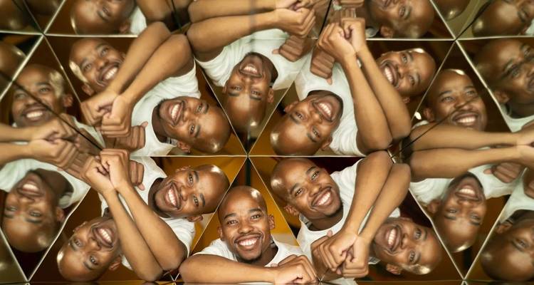Man smiling surrounded by reflections in a kaleidoscopic display.