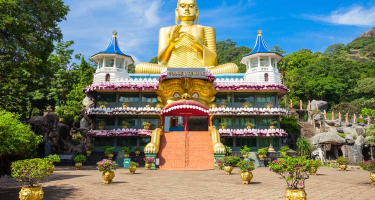 Strahlend goldener Buddha überragt die farbenfrohe Fassade des Goldenen Tempels von Dambulla.