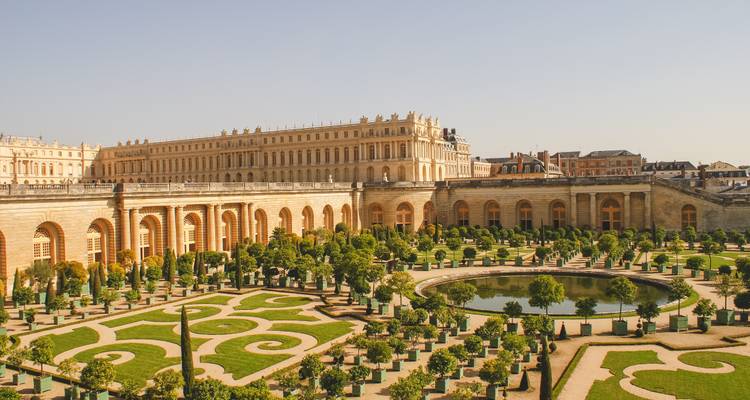 Jardines ornamentados y arquitectura del Palacio de Versalles bajo un cielo despejado.