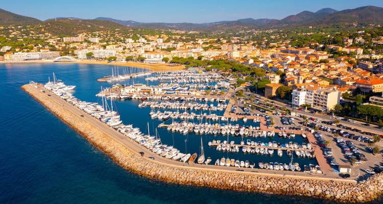 Panorama aéreo del puerto deportivo de Saint-Tropez con filas de yates y tejados de terracota respaldados por colinas.